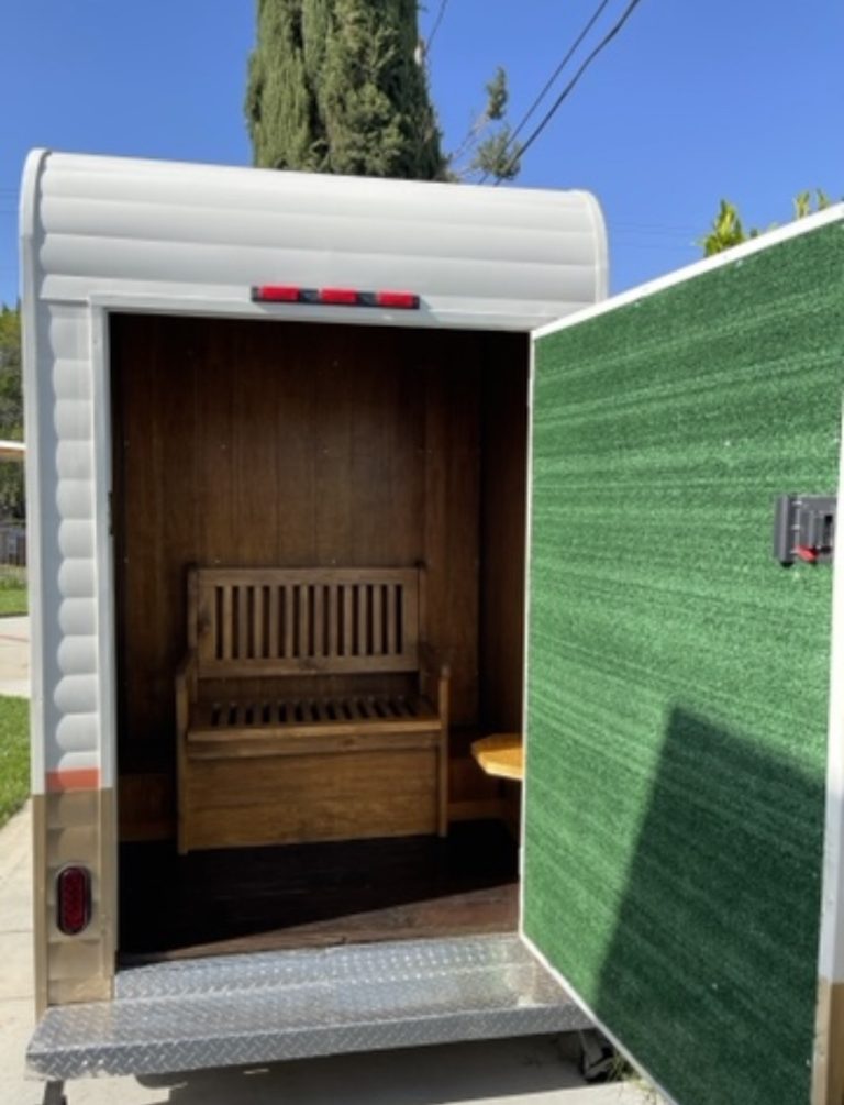 The back of a beer tap trailer. The interior is wooden, with a slatted bench. The interior of the door is layered in a green carpeted texture.